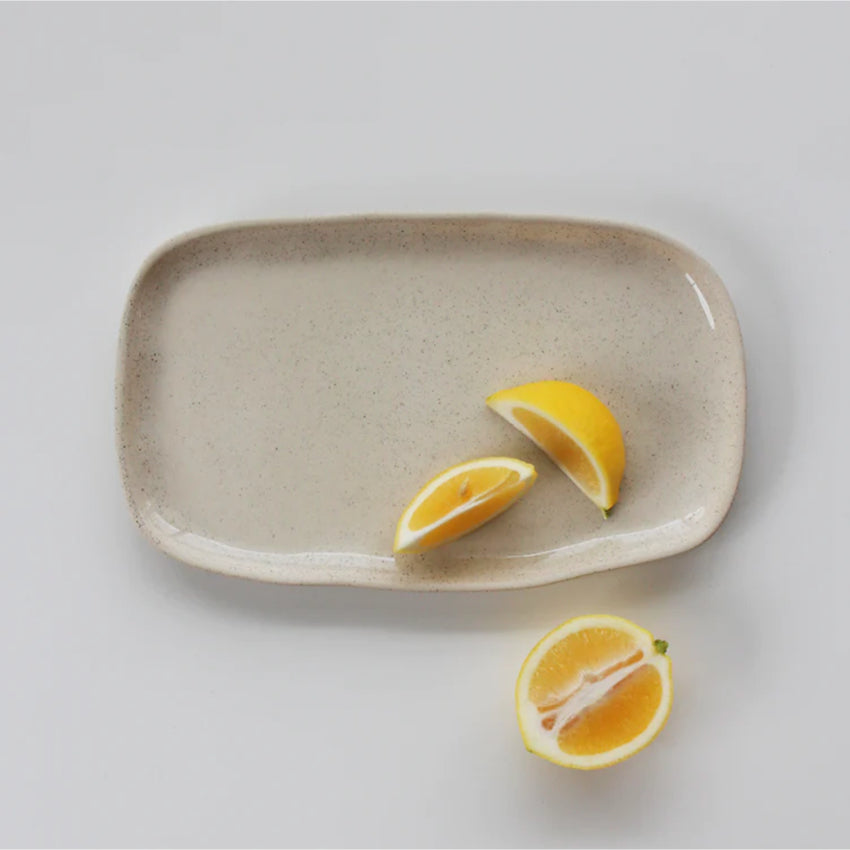The JS Ceramics Rectangle Platter in Oatmeal with lemon slices on it on a blank background