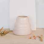 The JS Ceramics Wave Vase in Pink Sand with leaves and flowers and a wooden spoon next to it