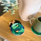 Three of the Kathryn Furniss Coasters on a table, one with a mug on it