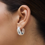 The La Tribe Half Moon Hoops in Silver on a womans ear.