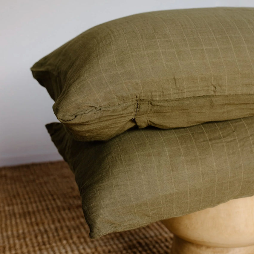 Leni The Label Muslin Pillowcases in Olive stacked on a stool