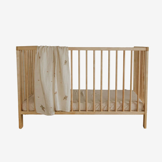 Leni The Label Muslin Swaddle in Kanuka hanging over a crib on a blank background