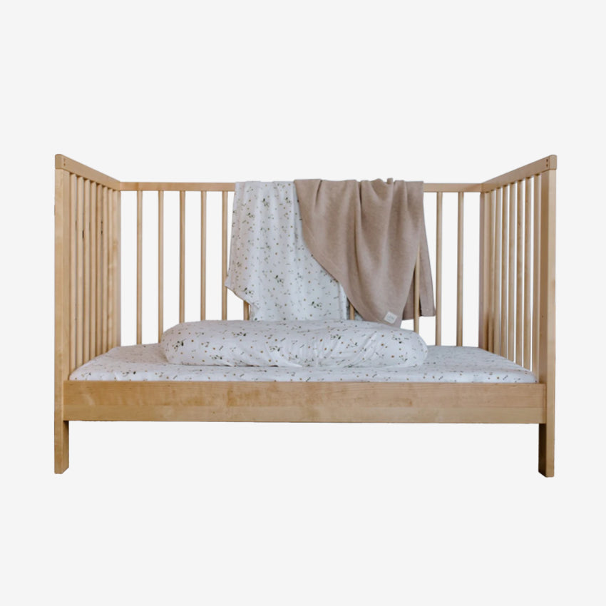 The Leni The Label Muslin Swaddle in Daisy hanging over a crib on a blank background