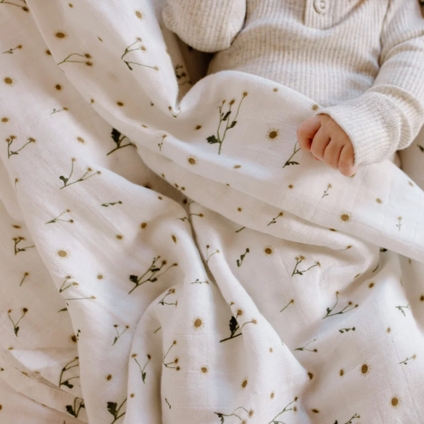 The Leni The Label Muslin Swaddle in daisy with a baby wrapped in it 