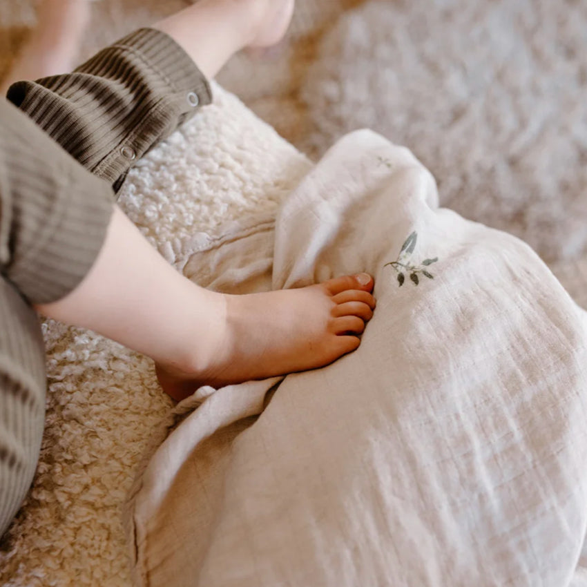 The Leni The Label Muslin Swaddle in Gum laying over a couch with a kid