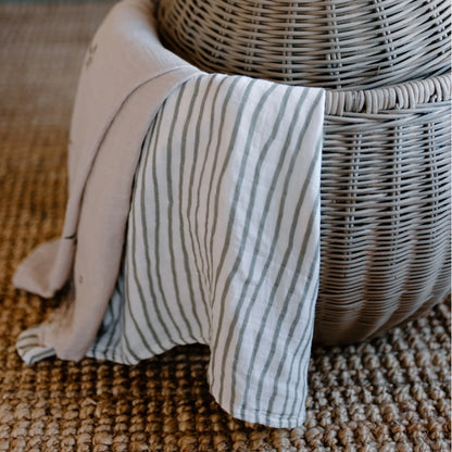 The Leni The Label Muslin Swaddle in Moss Stripe hanging out of a basket