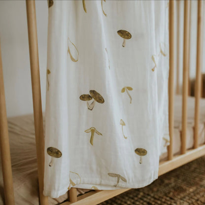 The Leni The Label Muslin Swaddle in Mushroom hanging over a crib