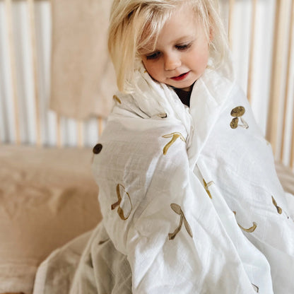 The Leni The Label Muslin Swaddle in Mushroom with a kid wrapped up in it