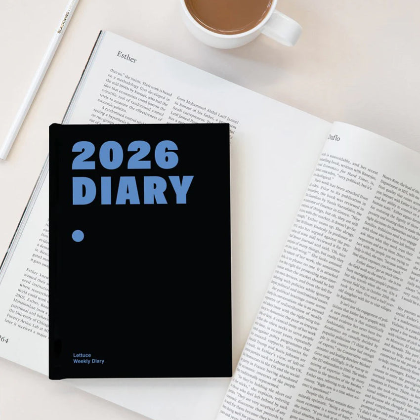 The Lettuce 2026 Weekly Diary in Midnight on top of a magazine and next to a pencil and coffee