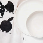 The Lettuce Linen Tea Towel in Fruit Shelf design under white plates