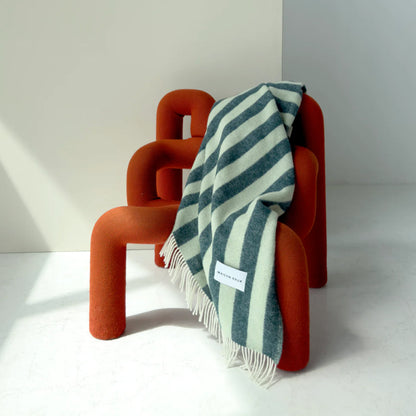 Orange chair with a Maison Deux Candy Wrap Blanket in Green Sage draped over it on a white background