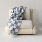 Beige armchair with Maison Deux Checkerboard blanket in Denim draped over it on a light gray background