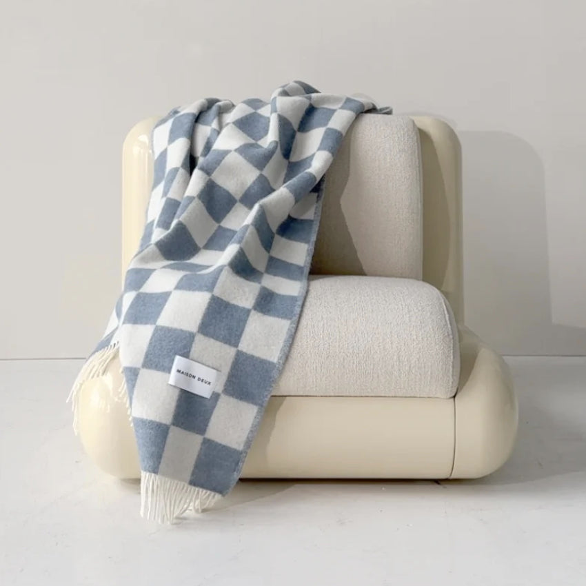 Beige armchair with Maison Deux Checkerboard blanket in Denim draped over it on a light gray background