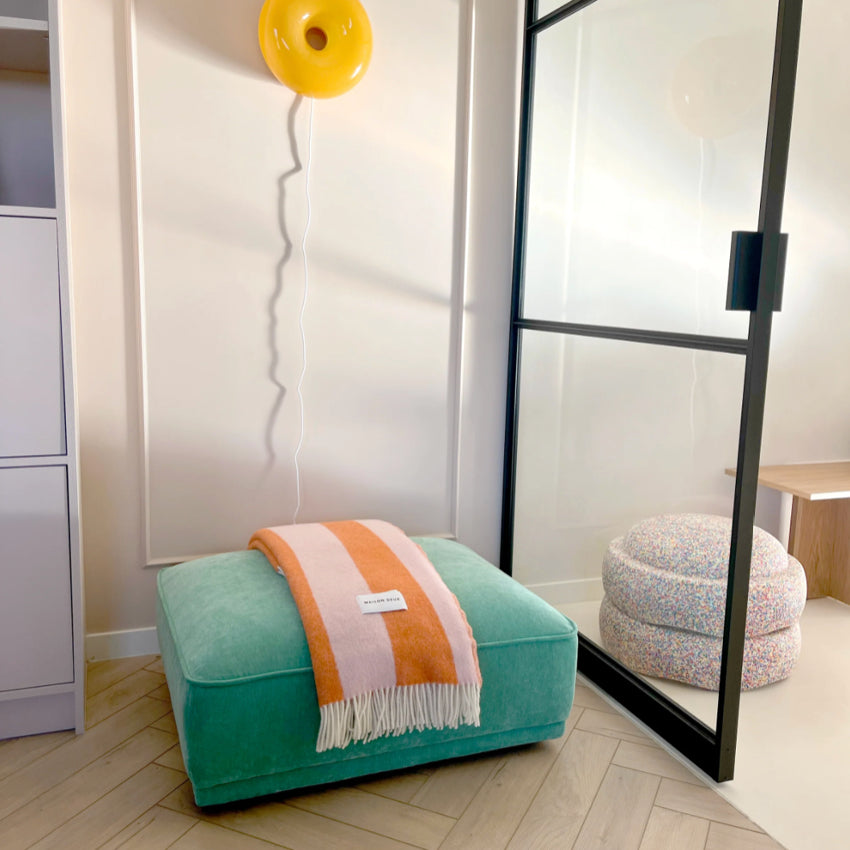Teal ottoman with Maison Deux Rough Stripe Blanket in pink and orange blanket with in a modern room.