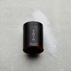 The Matakana Essentials Magnesium Bath Salts 500g jar on concrete with salts next to it