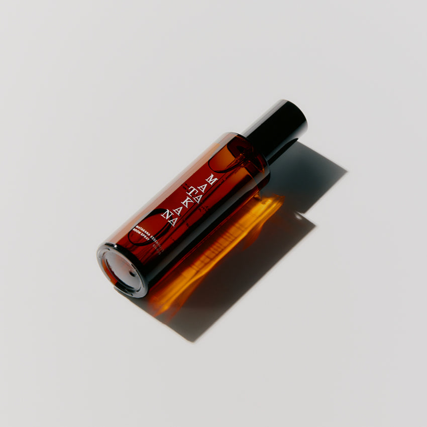 The Matakana Essentials Room Spray brown bottle lying down on a grey background