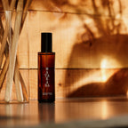 The Matakana Essentials Room Spray brown bottle on a benchtop next to a vase of sticks