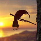 The Metalbird Huia Garden Sculpture in a tree with a sunset background