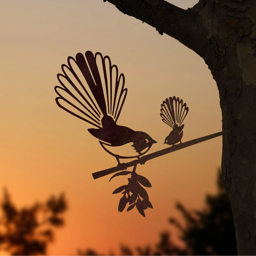 The Metalbird steel Piwakawaka and Baby in a tree with a sunset background
