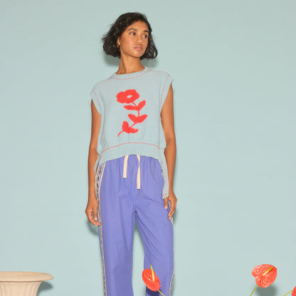 The Nancybird Aria Vest in Flower on a model paired with track pants on a blue background