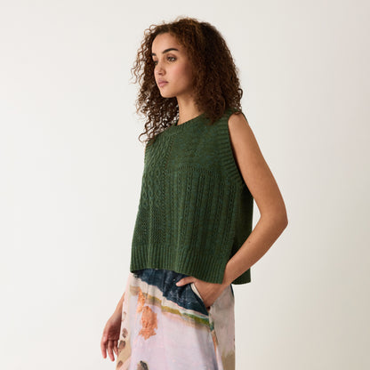 A side view of the Nancybird Billie Cable Vest in Cypress Green on a model on a grey background