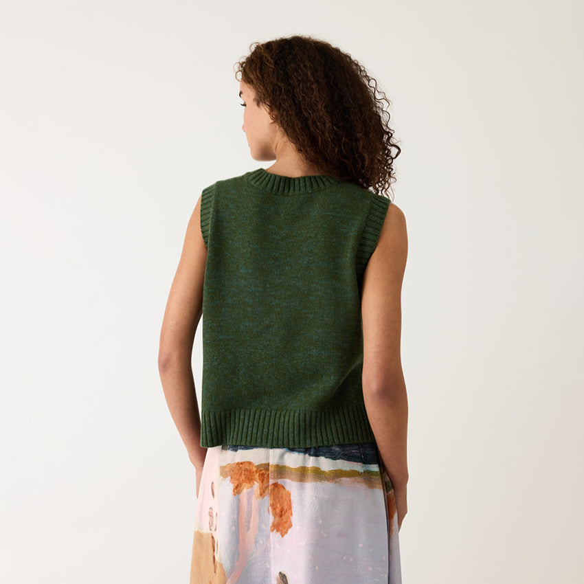 A back view of the Nancybird Billie Cable Vest in Cypress Green on a model on a grey background