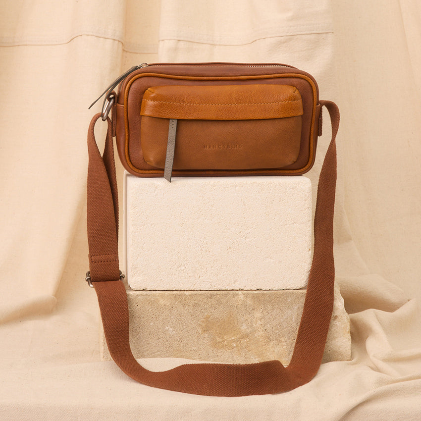 The Nancybird Goshen Bag in Tan on a brick in front of material
