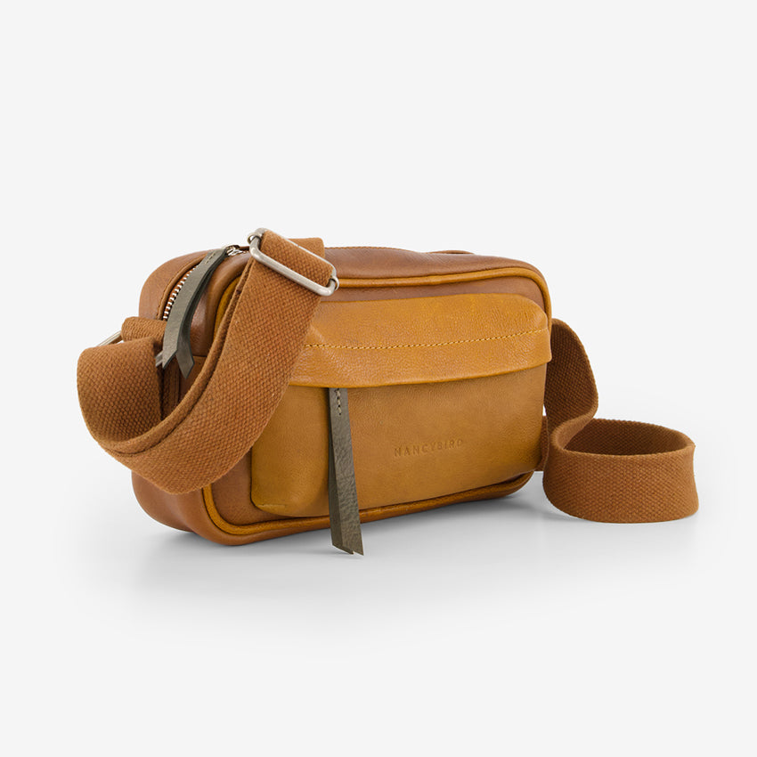 A side view of the Nancybird Goshen Bag in Tan on a grey background
