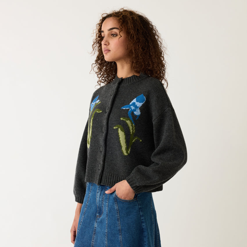 A model wearing the Nancybird Iris Cardigan, turned to the side on a grey background