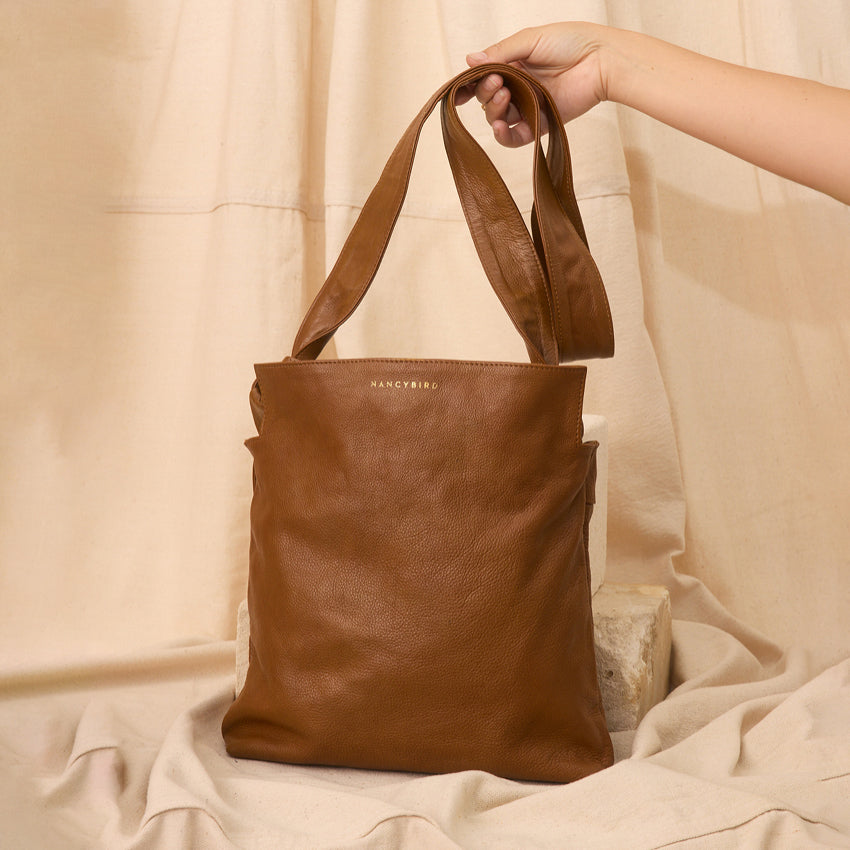 The Nancybird Shiki Bag in Tapenade with the strap being held up with a cloth background