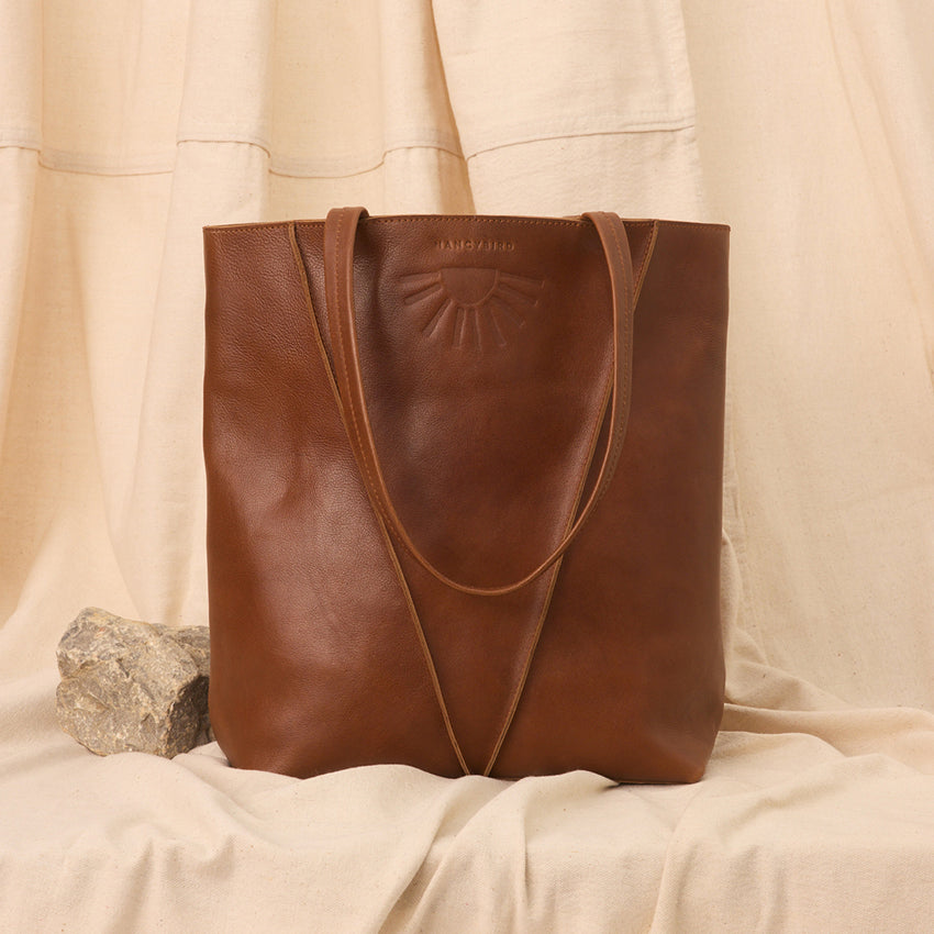The Nancybird Tri Tote in Tobacco on fabric next to a rock