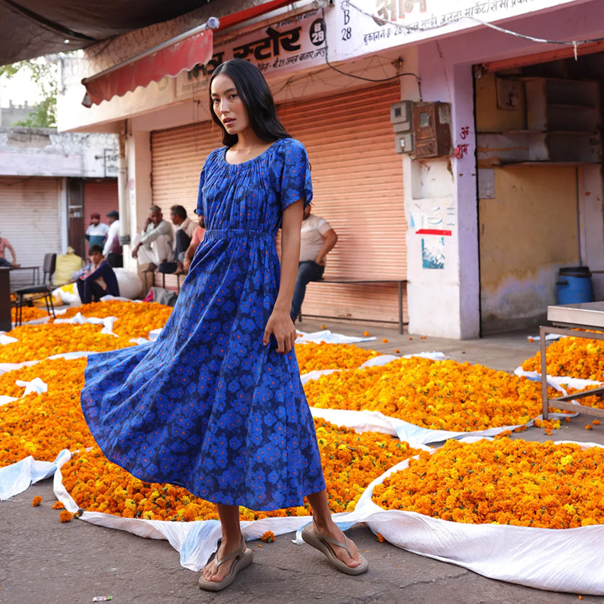 The Nancybird Daphne Dress in Midnight Floral on a model with flowers behind her