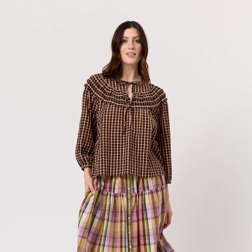 The Nancybird Jira Pintuck Blouse in Jaipur Check on a model paired with a skirt on a blank background