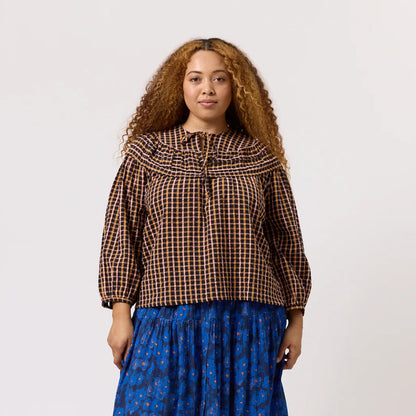 The Nancybird Jira Pintuck Blouse in Jaipur Check on a model paired with a skirt on a blank background