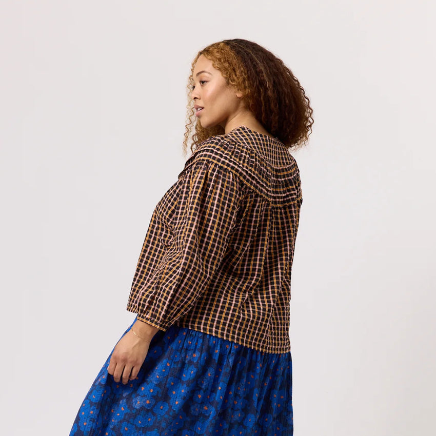 A view of the back of the Nancybird Jira Pintuck Blouse in Jaipur Check on a model paired with a skirt on a blank background