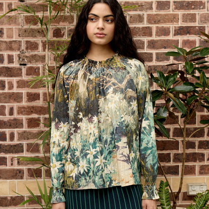 The Nancybird Rowena Shirred Blouse in Flannel Flower on a model against brick and greenery 