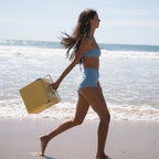 The Napoleon Goods Mini Chilly Bin in Lemon Yellow with a girl in a bikini holding it on a beach