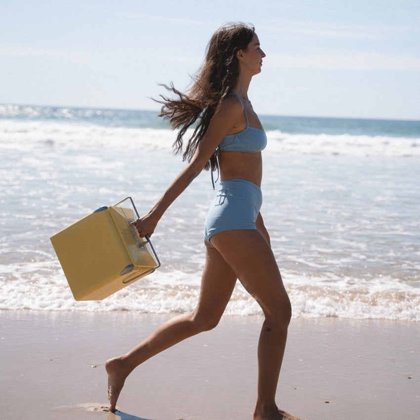 The Napoleon Goods Mini Chilly Bin in Lemon Yellow with a girl in a bikini holding it on a beach