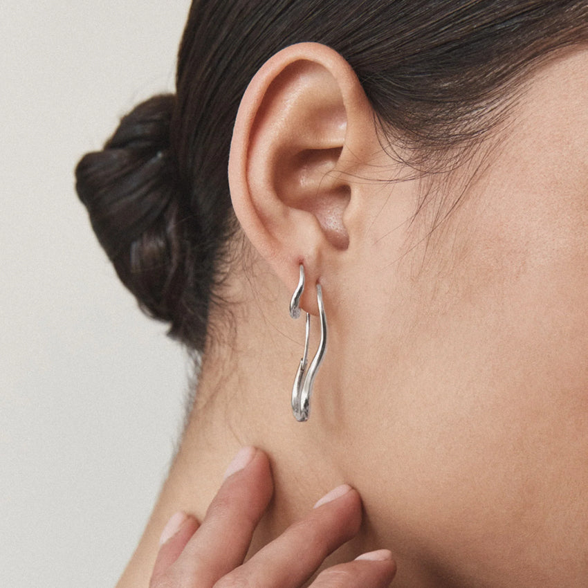 The Nina Gordon Ventee Hoops in Silver on a model paired with another earring