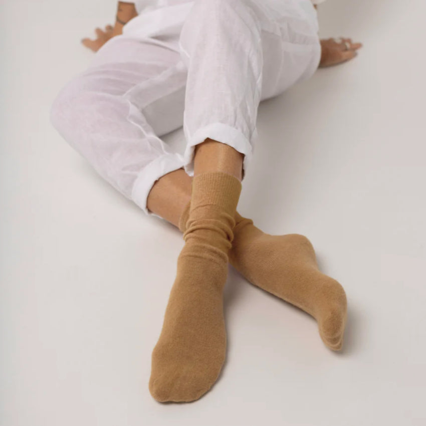Person wearing white pants and beige Hamilton Possum and Merino Wool socks on a light background