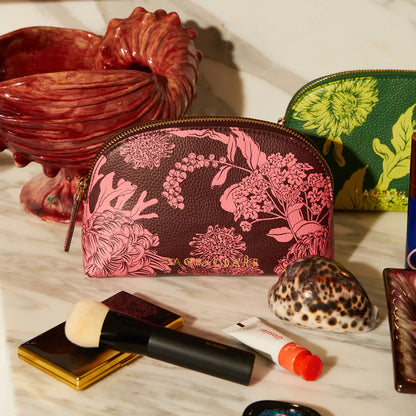 The Sage x Clare Delphine Cosmetic Pouch in Garnet on a vanity next to shells and makeup