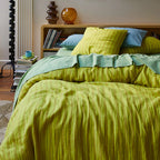 The Sage x Clare Nadine Linen Duvet Cover in Olive on a bed with striped sheets and cushions
