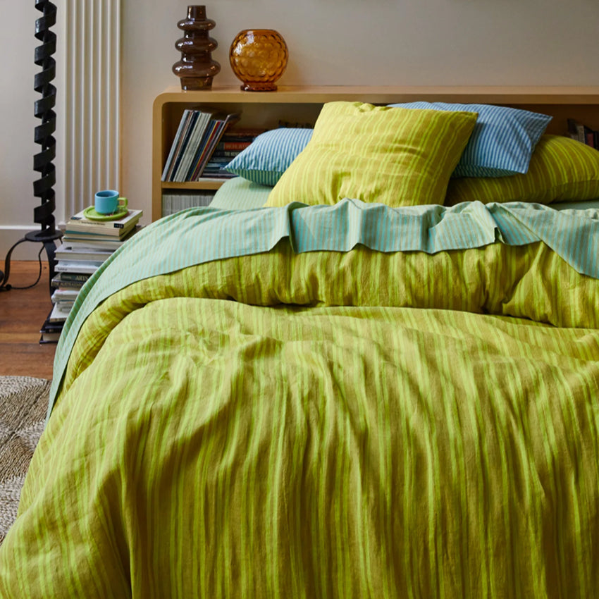 The Sage x Clare Nadine Linen Duvet Cover in Olive on a bed with striped sheets and cushions