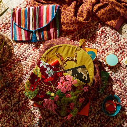 The Sage x Clare Genevieve Velvet Clutch open with items in it on a rug