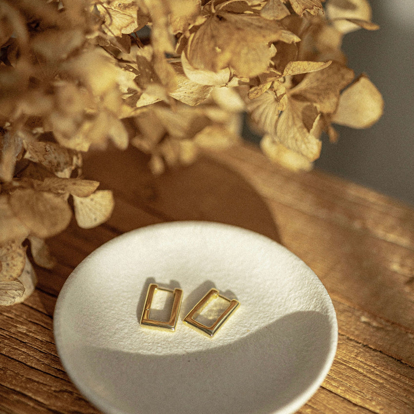 The Silver Linings Collective Avery Earrings in Gold on a dish next to flowers