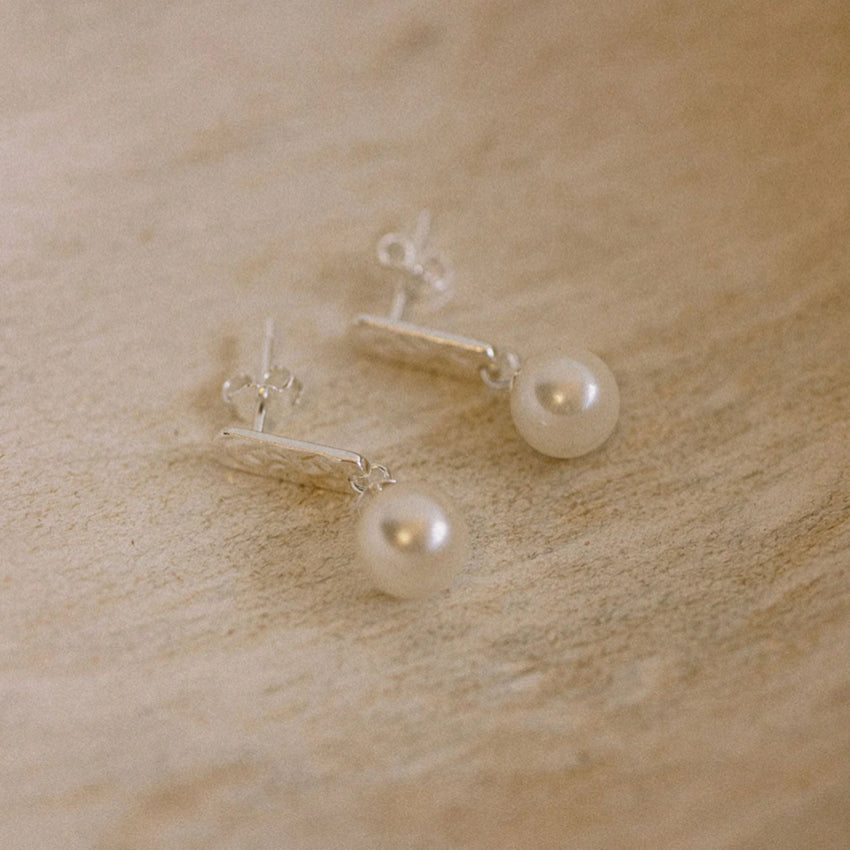 The Silver Linings Collective Luna Pearl Earrings in Silver on a textured background