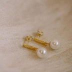 The Silver Linings Collective Luna Pearl Earrings in Gold on a textured background