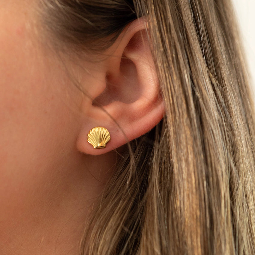 The Silver Linings Collective Shell Studs in Gold on a models ear