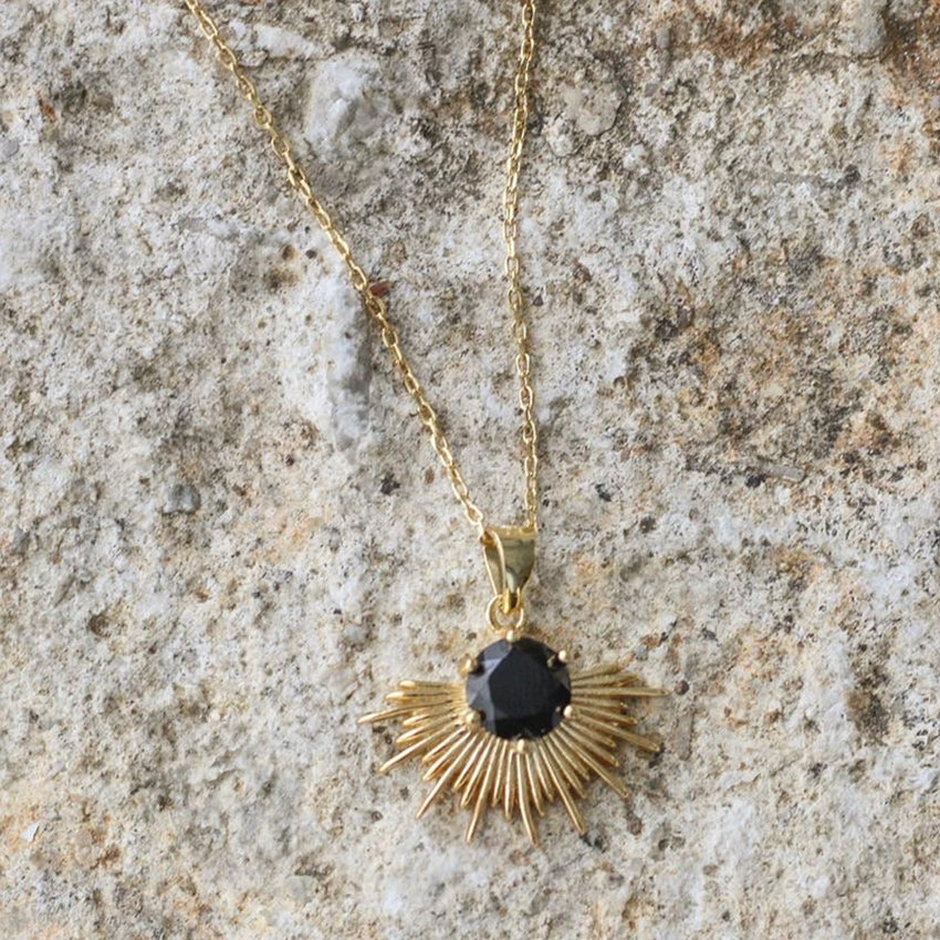 The Silver Linings Collective Solace Necklace in Gold on a textured background