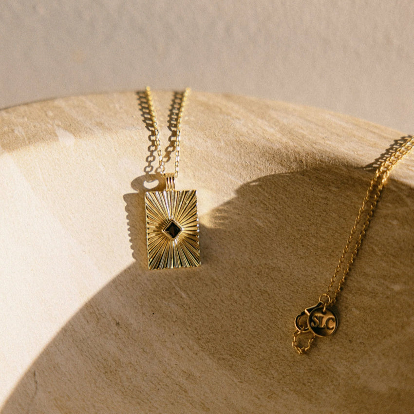The Silver Linings Collective Verity Necklace in Gold on a textured bowl.